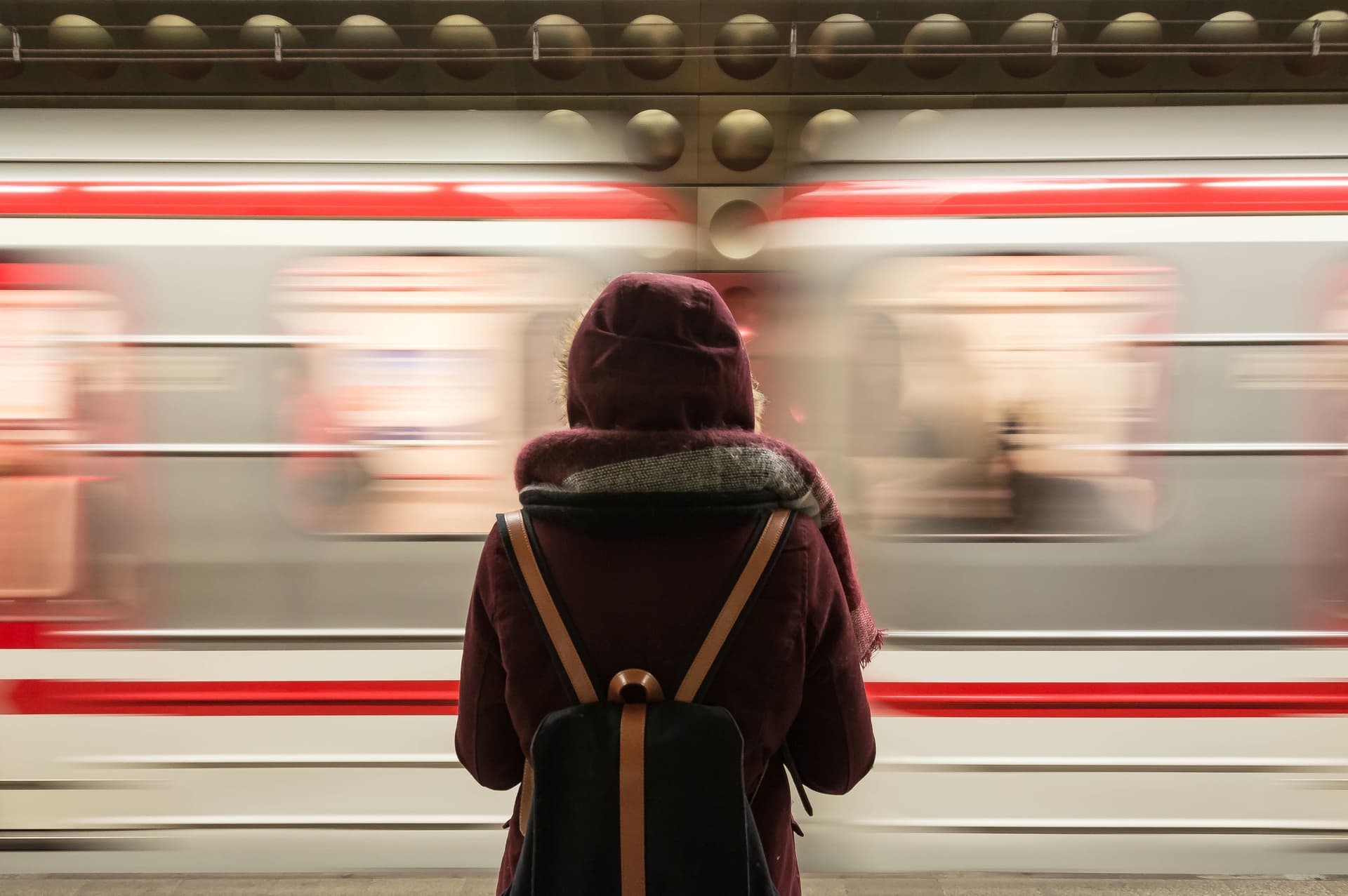 Une femme de dos avec un sac à dos devant un train