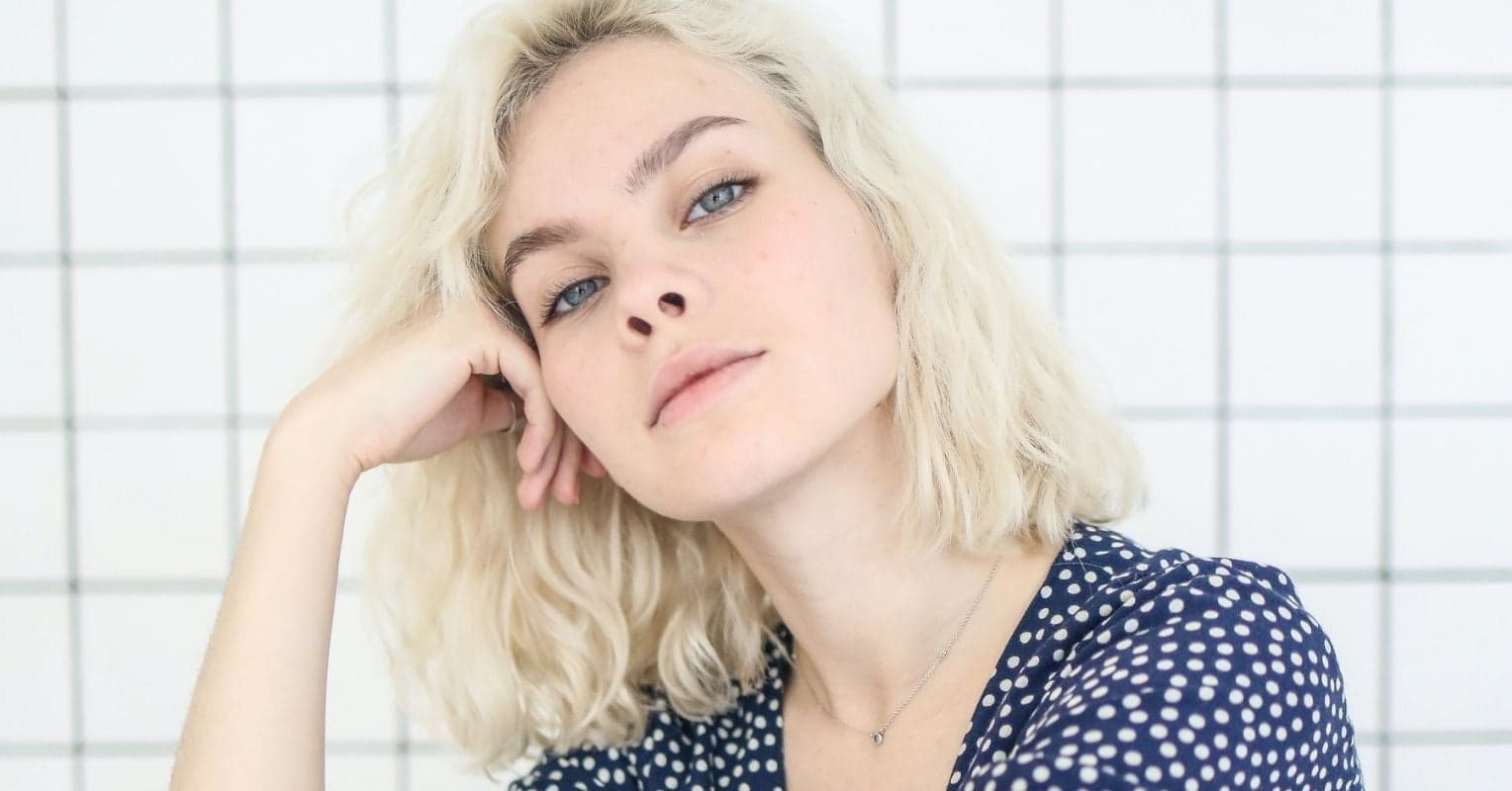 A blond woman seating backwards on a chair looks at the camera