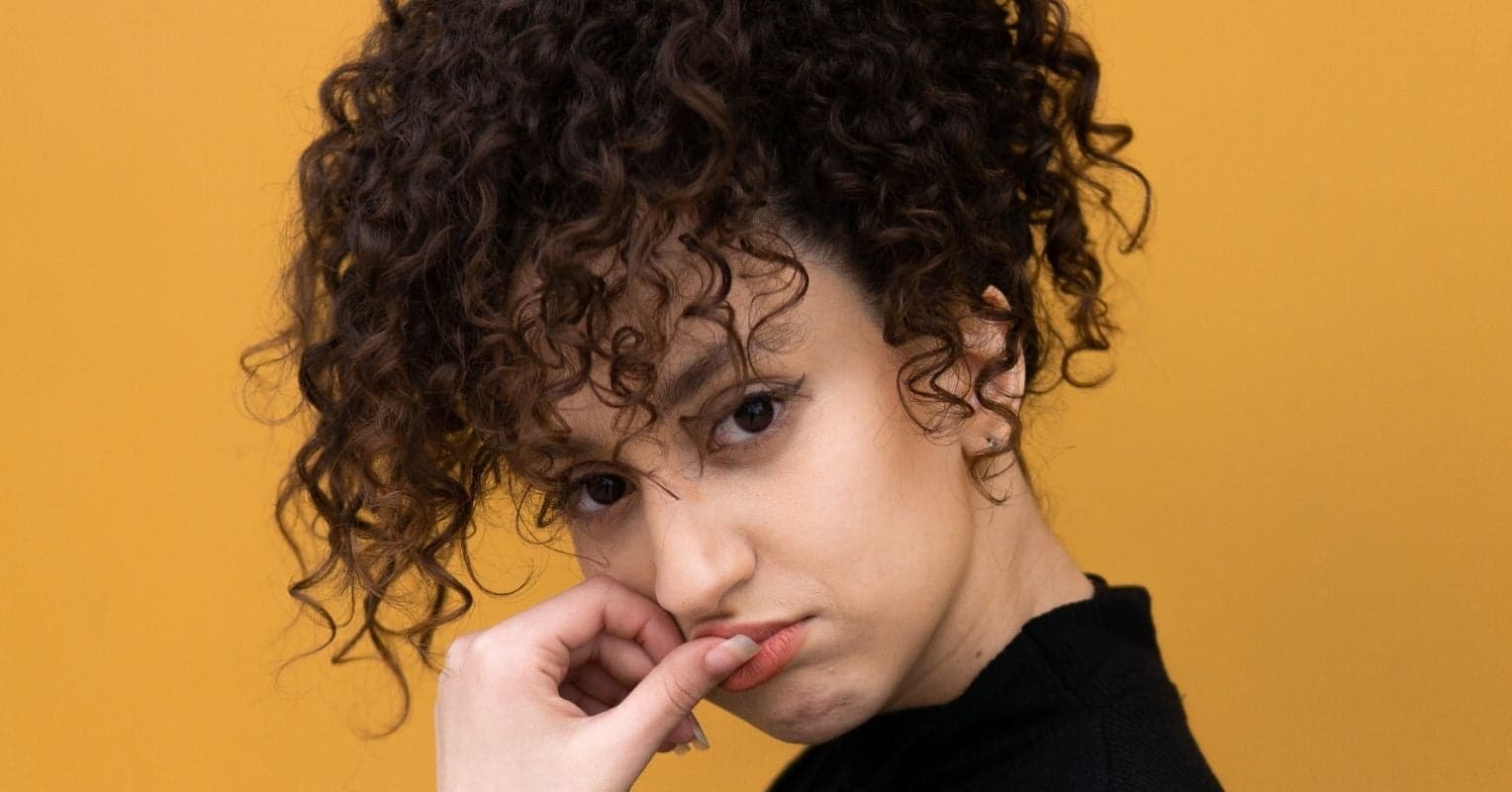 A young woman with curly hair in front of a yellow background