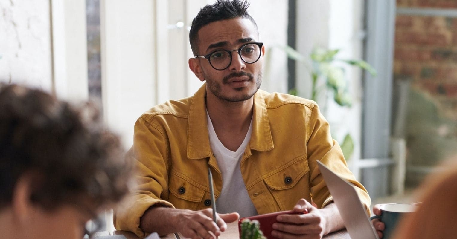Un jeune homme avec des lunettes et une veste jaune à une réunion