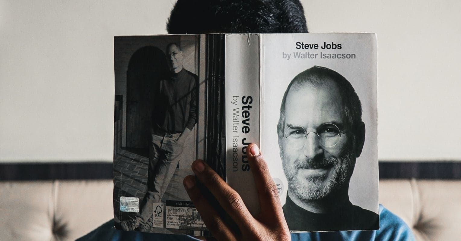 Un homme dont le visage est caché par la biographie de Steve Jobs